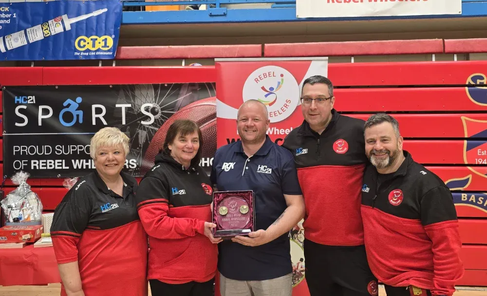 group of five rebel wheelers volunteers and staff with patron posing with a award plaque