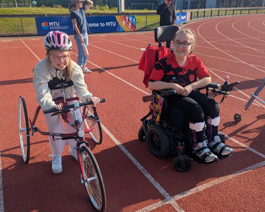 two female para athletics junior athletes, one on a bike and the other in a wheelchair on a track